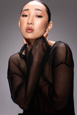 Asyalı kadın, fotoğraf makinesi için poz verirken ellerini yüzüne koydu.