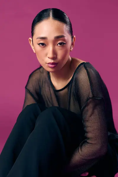 stock image Fashion asian woman sitting on a purple background in a sheer top and black pants with her eyes closed and hands on her knees.