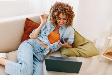 Modern oturma odasında dizüstü bilgisayarda çalışan gülümseyen kadın.