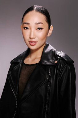 Moda, Asyalı kadın, siyah deri ceket, stüdyo resmi, gri arka plan. Tarz sahibi Asyalı bir kadın, gri arka planda siyah deri ceket giyen bir stüdyo resmine poz veriyor..