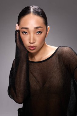 Gri arkaplan önünde poz veren katıksız bluzlu moda Asyalı kadın..