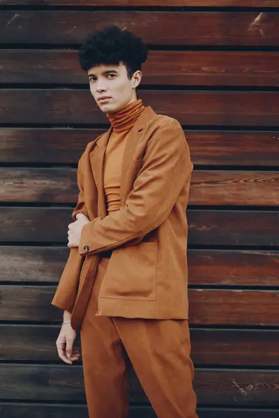 stock image A fashionable young man stands confidently in a brown suit, with a textured wooden background enhancing his attire