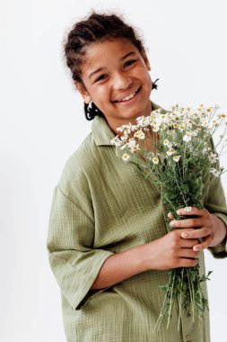 Neşeli genç bir çocuk elinde bir buket papatya tutuyor, basit bir beyaz arka plana karşı masumiyet ve mutluluk yayıyor..