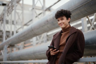 Şehirde endüstriyel bir binanın önünde cep telefonunu kullanan Afro-Amerikan bir kadının moda portresi..