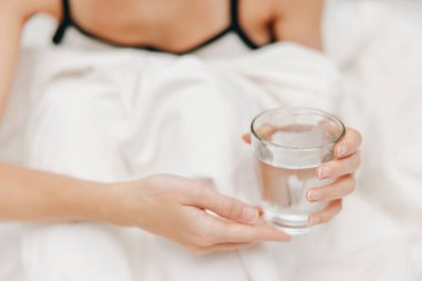 İki bardak suyla yatakta yatan kadın, battaniyeyle örtülmüş..