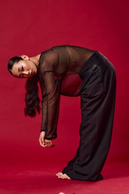 Siyah pantolonlu moda Asyalı kadın ve kırmızı arka planda tenis topunu kaldıracak kadar bükülüyor..