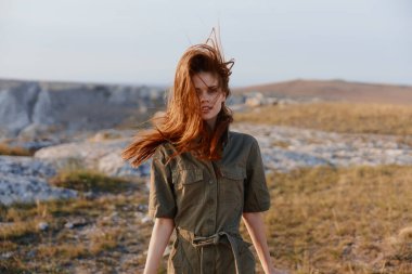 Uçan kızıl saçlı bir kadın rüzgar esintisi, doğanın güzelliği ve özgürlük kavramı ile canlı bir tarlada duruyor.