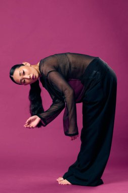 Üstü açık Asyalı moda kadını ve mor arka planda eğilen siyah pantolonlu, elleri dizlerinin üstünde ve başı yana yatmış..