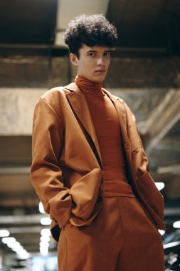 Aynı turuncu takım elbise ve balıkçı yaka giyen, moda ve yaşam tarzı için ideal endüstriyel bir geçmişe sahip, kendine güveni ve tarzı olan şık genç bir adam.