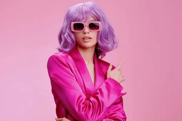 stock image Woman in pink suit and sunglasses on pink background, hand on face, looking at camera