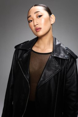 Stüdyoda gri arka planda poz veren siyah deri ceketli Asyalı kadın..