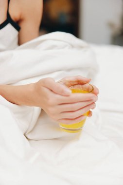 Yatağında beyaz çarşaf ve yorganla bir fincan portakal suyu taşıyan bir kadın..