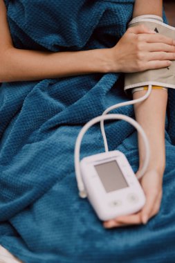 Mavi battaniyeli kişi, mavi battaniyeli başka bir kişinin önünde kan basıncı monitörü ve elektronik cihazı tutuyor..