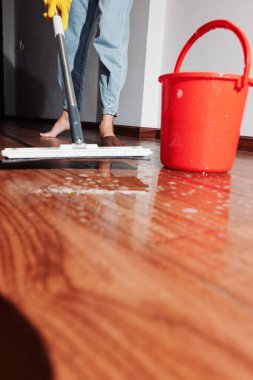 Ahşap zemini paspas ve bir kova suyla temizleyen bir kadın. Profesyonel temizlik hizmeti konsepti. Temiz ve parlak ahşap yüzey. ev işleri ve ev işleri.