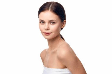 Beyaz kolsuz tişörtlü genç bir kadın gülümsüyor ve elleri kalçasında kameraya poz veriyor..