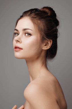 Elleri kafasında gri arka planda poz veren genç bir kadın. Güzel ve kendinden emin bir ifade. Model fotoğraf çekimi konsepti.