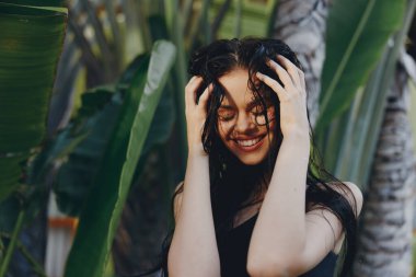 Tropik bir sahil tatilinde palmiye ağacının önünde poz veren uzun siyah saçlı şık bir kadın.