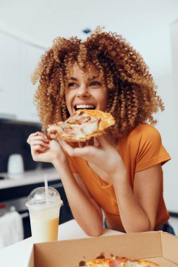 Mutlu kadın güneşli bir günde karton bir kutunun önünde lezzetli bir dilim pizzanın tadını çıkarıyor.