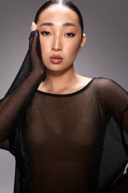 Elleri yüzlerinde pozlar veren, katıksız bluzlu, moda Asyalı kadın. Kameraya bakan şeffaf bluzlu, şık Asyalı genç bir kadının portresi..