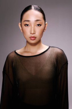 Gri arka planda poz veren üstü açık Asyalı bir kadın. Moda tarzı.