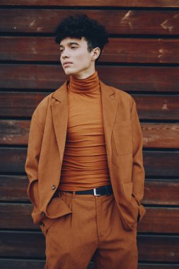 Modaya uygun genç bir adam zarif kahverengi bir elbise içinde, kırsal bir ahşap zemine karşı modern tarzını sergiliyor.