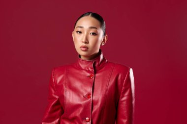Kırmızı arka planda poz veren kırmızı deri ceketli Asyalı kadın. şık ve güzel Asyalı güzelliği.