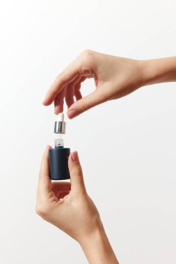 Beyaz arka planda küçük bir parfüm şişesi tutan iki el. Metin ya da logo için fotokopi alanı var. Güzellik ve parfüm kavramları için mükemmel basit ve zarif bir görüntü..