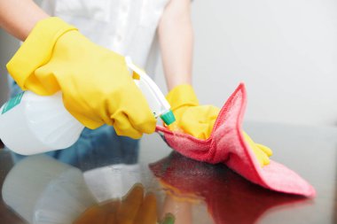 Tezgahta temizleme sehpası ve bez parçaları olan bir kadın. Ellerinde sarı eldivenler.