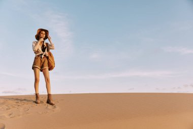 Sırtında bir çantayla kum tepesinde duran bir kadın panoramik çöl manzarasına hayran.