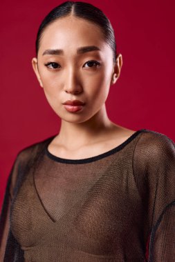 Kırmızı arka planda poz veren katıksız bluzlu Asyalı bir kadın. Zarif ve şık bir genç hanımın, cesur ve kendine güvenen bir görünüşü var. Güzellik ve moda kavramları için mükemmel..