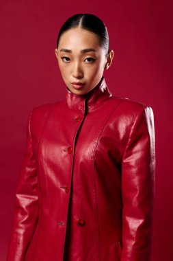 Kırmızı arka planda poz veren kırmızı deri ceketli Asyalı kadın. şık ve şık güzellik konsepti.