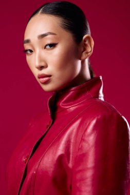 Kırmızı deri ceketli Asyalı esmer at kuyruklu kırmızı arka planda poz veriyor..