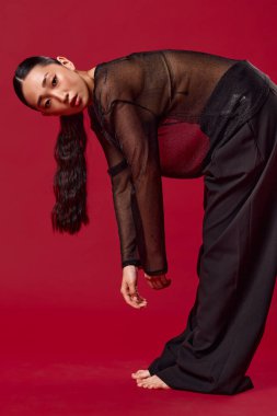 Siyah pantolonlu Asyalı bir kadın ve üstü açık kırmızı arka planda dizleri ve ayakları yere basan bir kadın. moda konsepti.