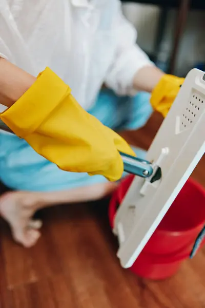 Stock image Woman cleaning floor with yellow gloves, mop, and bucket of water.