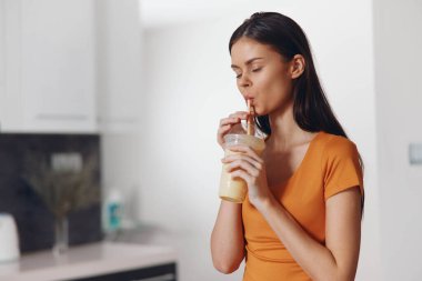 Modern mutfak ortamında beyaz tezgahlı sağlıklı meyve suyu içen bir kadın.