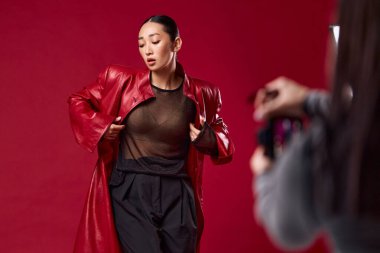 Kırmızı deri ceketli ve siyah pantolonlu Asyalı bir kadın kırmızı arka planda fotoğraf için poz veriyor. moda tarzı.
