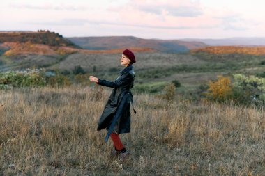 Siyah paltolu ve kırmızı şapkalı zarif kadın geniş alanda tek başına duruyor, engin boşlukta gizem ve yalnızlık yayıyor..