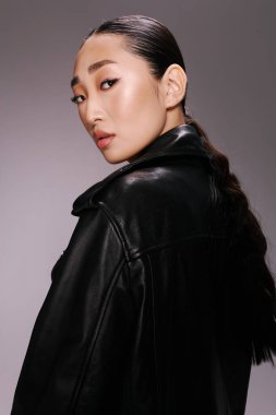 Siyah deri ceketli moda Asyalı kadın at kuyruklu kameraya poz veriyor..