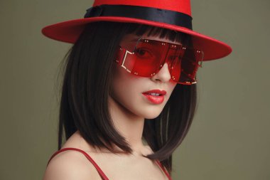 Kırmızı şapka, güneş gözlüğü, kadın, kırmızı şapka ve güneş gözlüğü takan bir kadın kendine güvenen bir duruş sergiliyor, bir elini kalçasına diğer elini de düşünceli bir şekilde çenesine koyuyor.