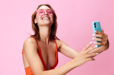 Modayı takip eden mayo giymiş neşeli bir kadın akıllı telefonuyla bir selfie çekiyor.