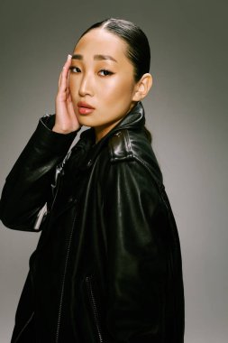 Moda Asyalı kadın siyah deri ceketi kameraya poz veriyor. Asyalı bir kadın şık siyah deri ceket giyiyor. Kamera görüntüsü için elleri yüzlerinde poz veriyor..