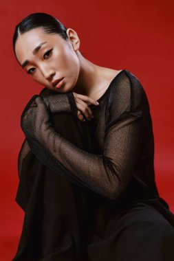 Siyah elbiseli Asyalı kadın kırmızı arka planda oturuyor elleri dizlerinde ve başı göğsünde dinleniyor. moda konsepti resmi.