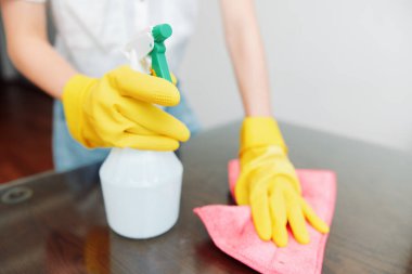 Sarı eldivenli kadın solüsyon ve tahta yüzey bezi kullanıyor..
