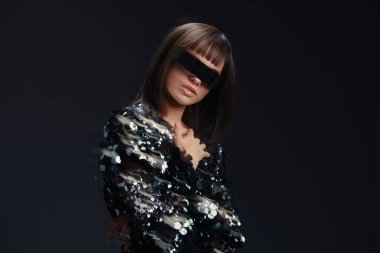 Kadın, güneş gözlüğü, pullu elbise şık güneş gözlüğü takan şık bir kadın ve parlak pullu bir elbise kalçasında elleriyle siyah bir arka plana karşı güvenli bir şekilde poz veriyor.