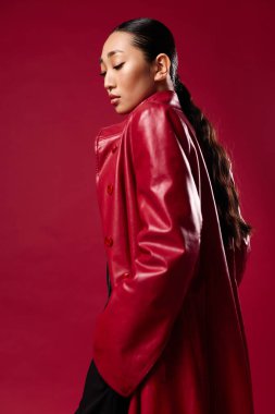 Beautiful asian woman in red leather coat and black pants posing against red background. fashion and beauty concept. clipart