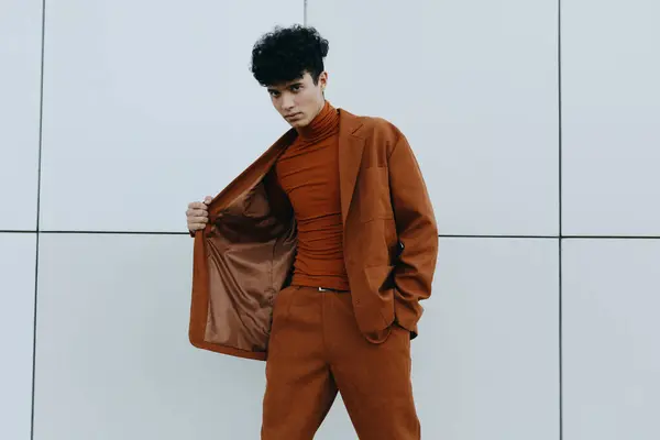 stock image A fashionable young man dressed in a rust suit with a matching turtleneck, striking a confident pose against a contemporary gray backdrop