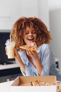 Mutlu bir kadın lezzetli bir dilim pizzanın ve gündelik ortamında kıvırcık saçlı taze bir milkshake 'in tadını çıkarıyor.