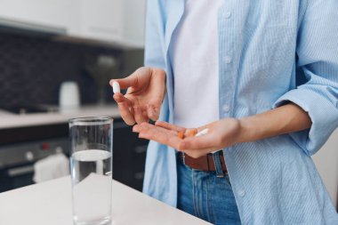 Evdeki mutfak tezgahında bir bardak suyla ilaç alan bir kadın.