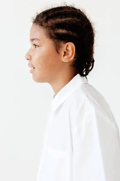 stock image Confident young boy with braids stands tall in a white shirt against a clean white background, showcasing style and self-assurance.