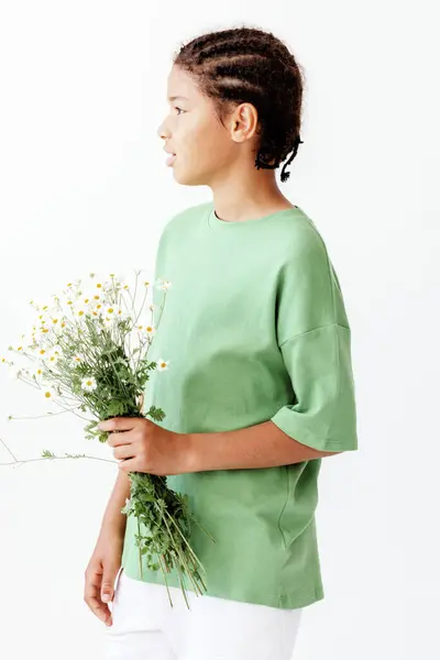 stock image Young boy in a trendy outfit holding a bouquet of daisies in a sunny field, radiating joy and innocence.